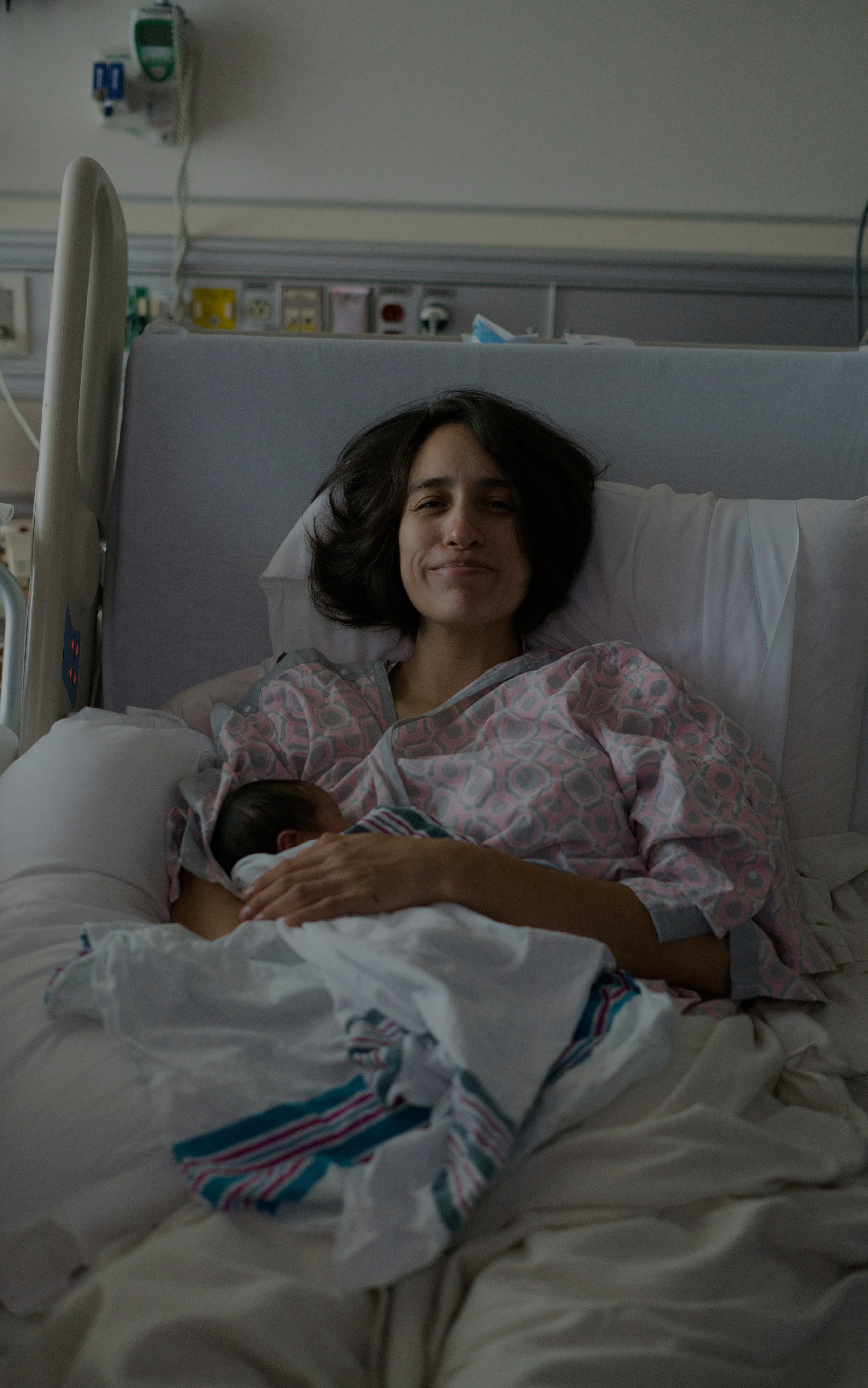 A mother sitting alone with her newborn, looking emotionally exhausted